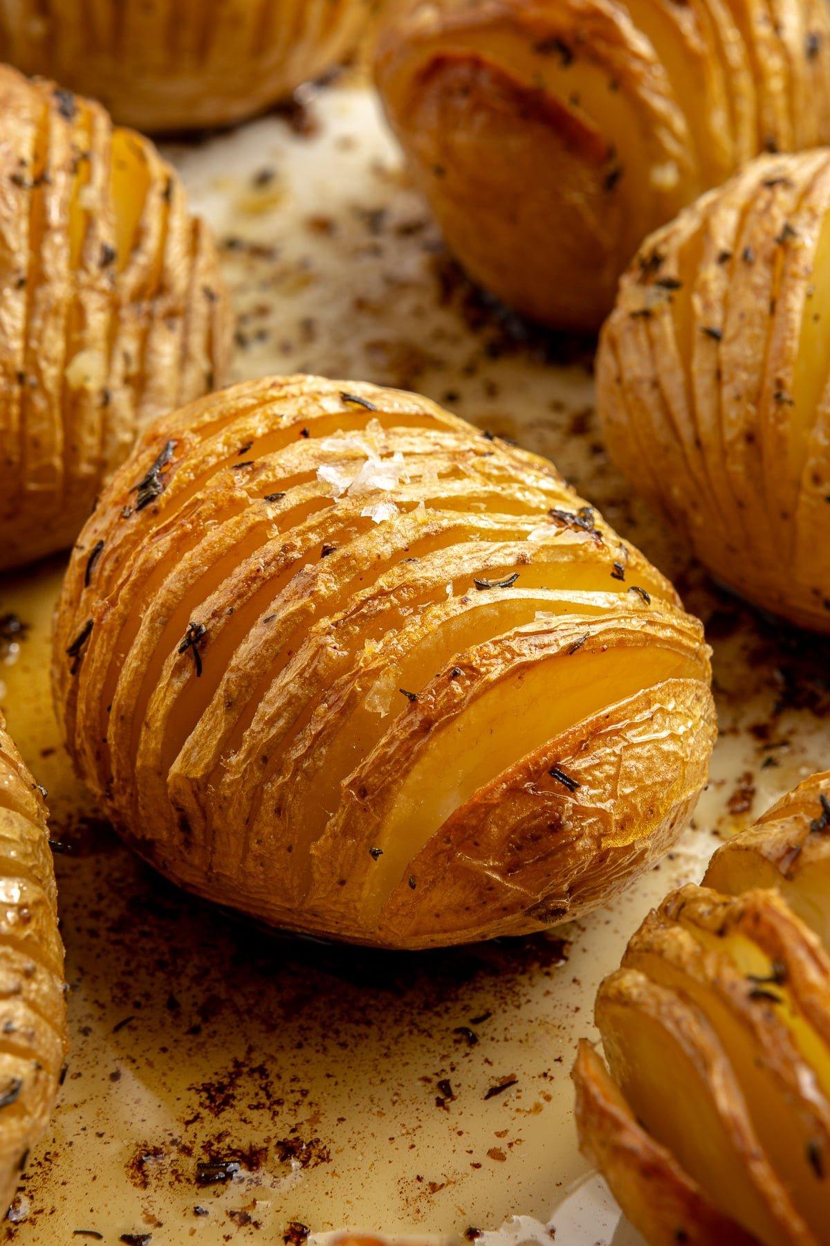 Hasselback-Kartoffeln mit Rosmarin 2 Fertig gebackene, goldbraune Kartoffeln liegen auf einem Backblech. Grobes Salz ist darüber gestreut.