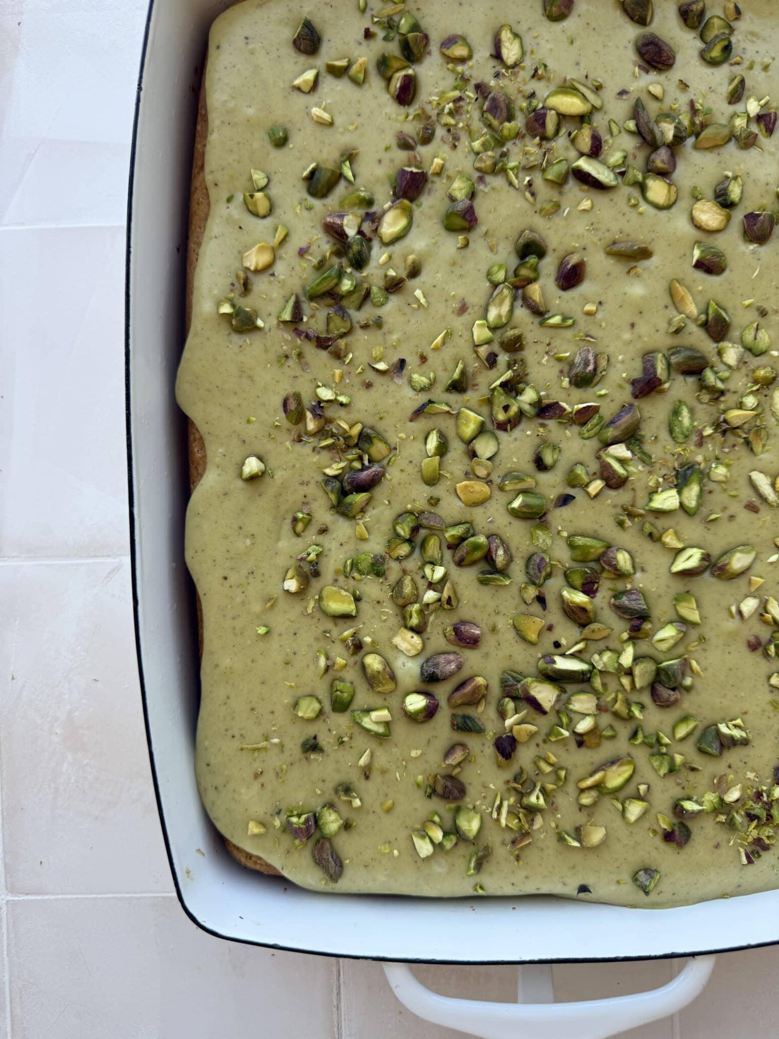 Pistazienkuchen mit Quarkcreme 2 Ein frisch gebackener Pistazienkuchen mit cremiger, hellgrüner Glasur, bestreut mit gehackten Pistazien. Ein Stück ist bereits herausgeschnitten und zeigt die saftige Textur.
