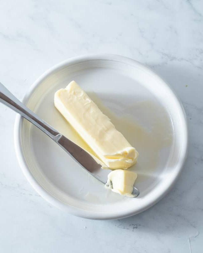 Butter schnell weich bekommen 2 Ein Stück weiche Butter auf einem kleinen weißen Teller mit einem Buttermesser daneben