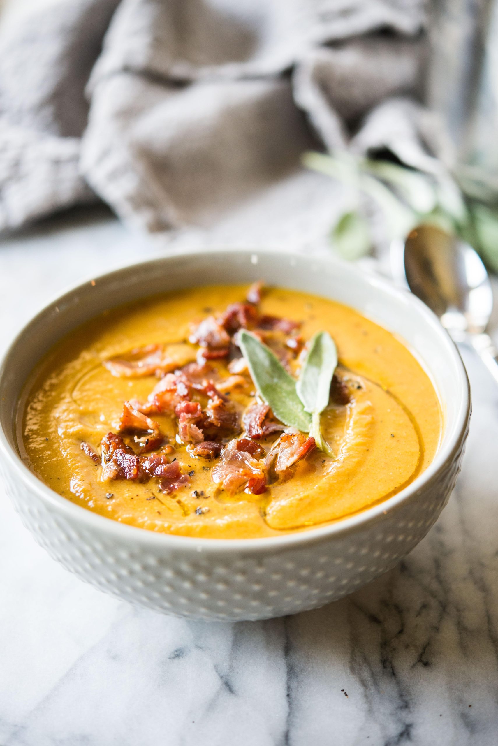 Graue Schüssel mit Instant Pot Kürbissuppe, belegt mit Speck und Salbei, auf einem Marmorbrett