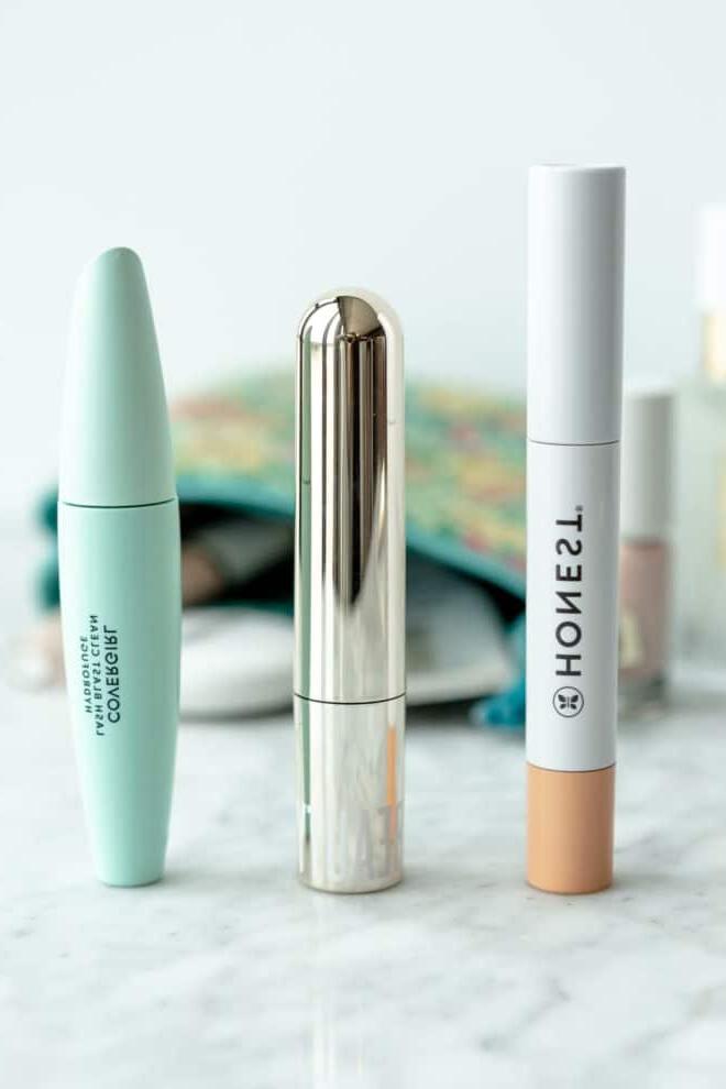 Beste Reine Mascara 2 Drei Wimperntuschen, die auf einer grau-weißen Marmoroberfläche aufgereiht sind, mit einer Kosmetiktasche im Hintergrund.