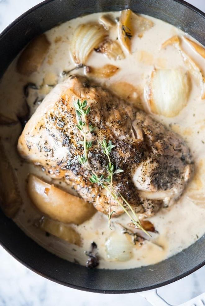 Apfelwein-Schweinebraten 2 Saftiger Schweinefiletbraten mit Apfelwein, umgeben von Äpfeln und Zwiebeln, auf einem Backblech angerichtet.