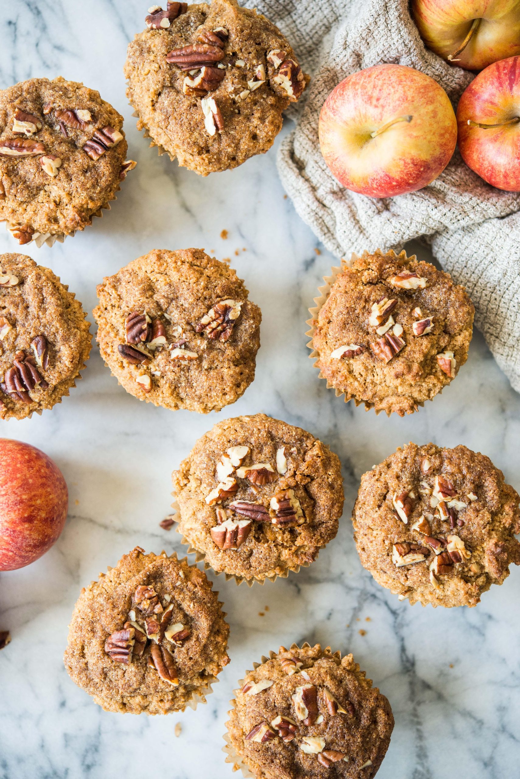 **Paläo Apfel-Zimt-Muffins** 2 paleo apple cinnamon muffins on a marble board surrounded by apples