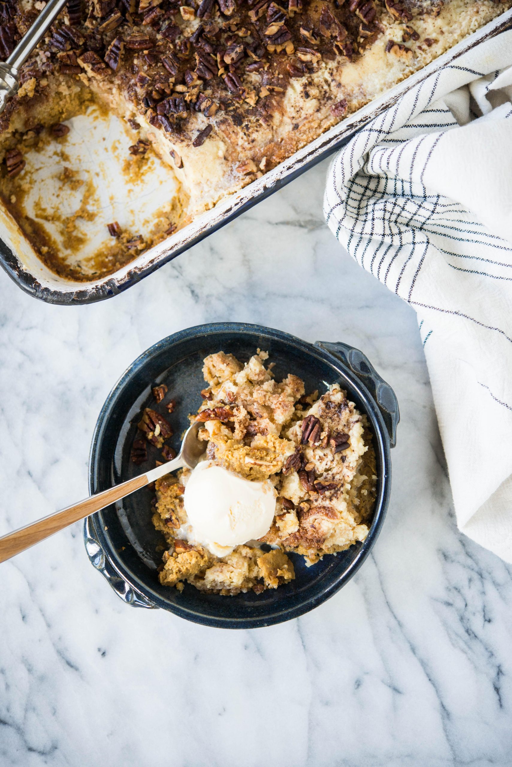 Kürbis-Dump-Kuchen 2 Dunkelblaue Schüssel mit Kürbis-Dump-Cake und einer Kugel Eiscreme darauf.