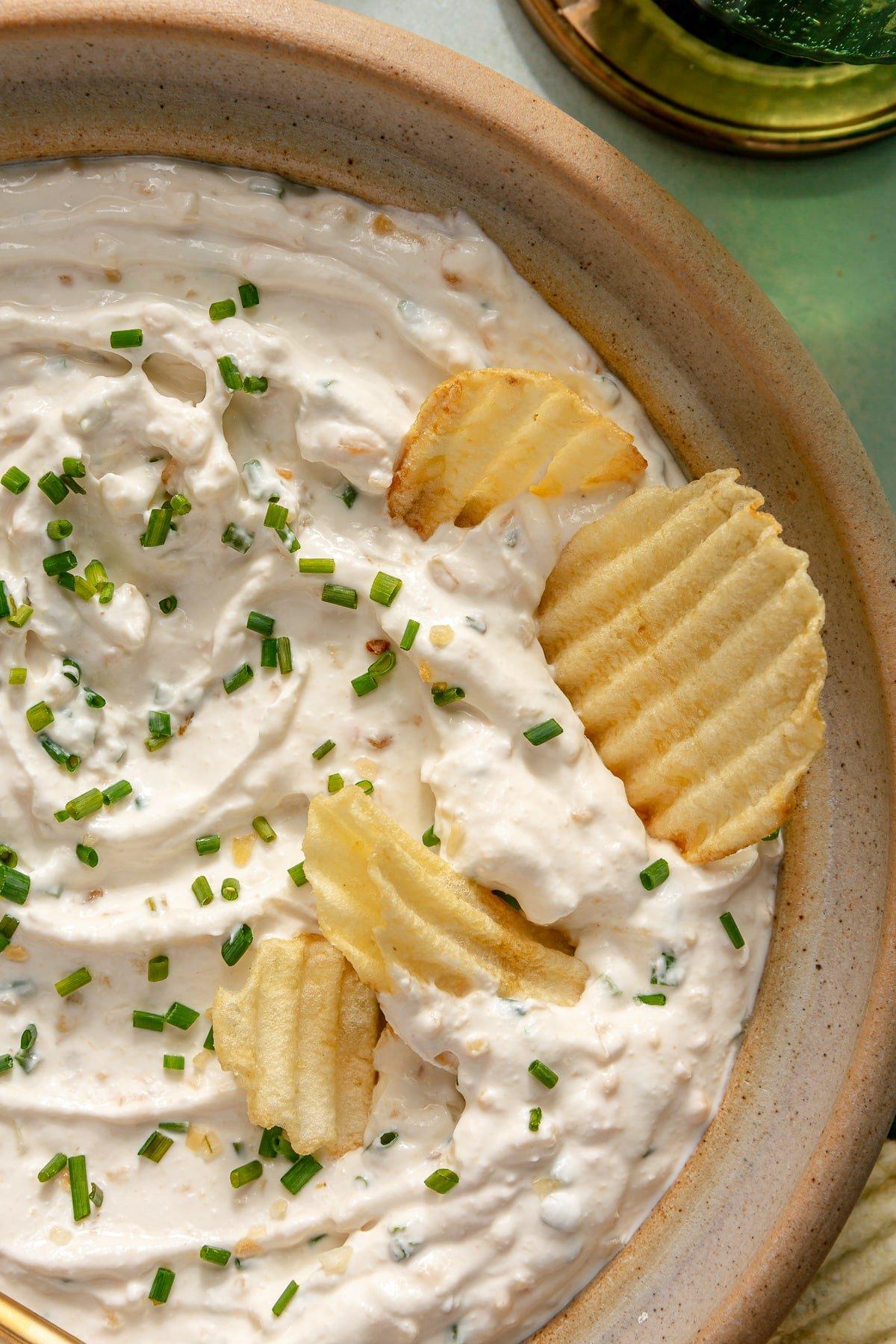 Eine Schüssel mit hausgemachtem Französischem Zwiebeldip, garniert mit frischem Schnittlauch und 4 Kartoffelchips, die im Dip stecken.