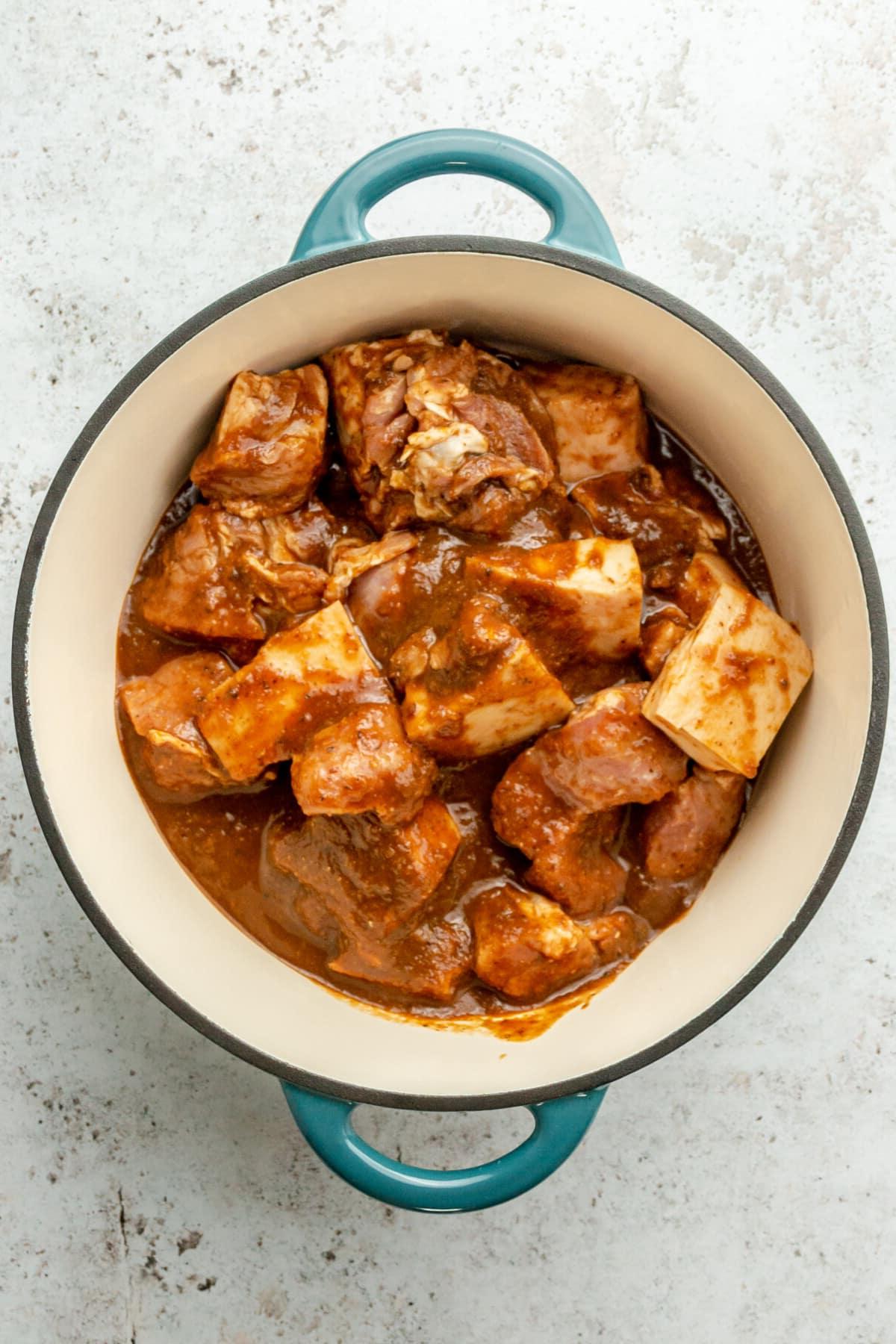 Tacos Al Pastor Rezept 11 Stücke von mariniertem Schweineschulterfleisch in einem emaillierten Gusseisentopf auf hellem Hintergrund, bereit für den Ofen.