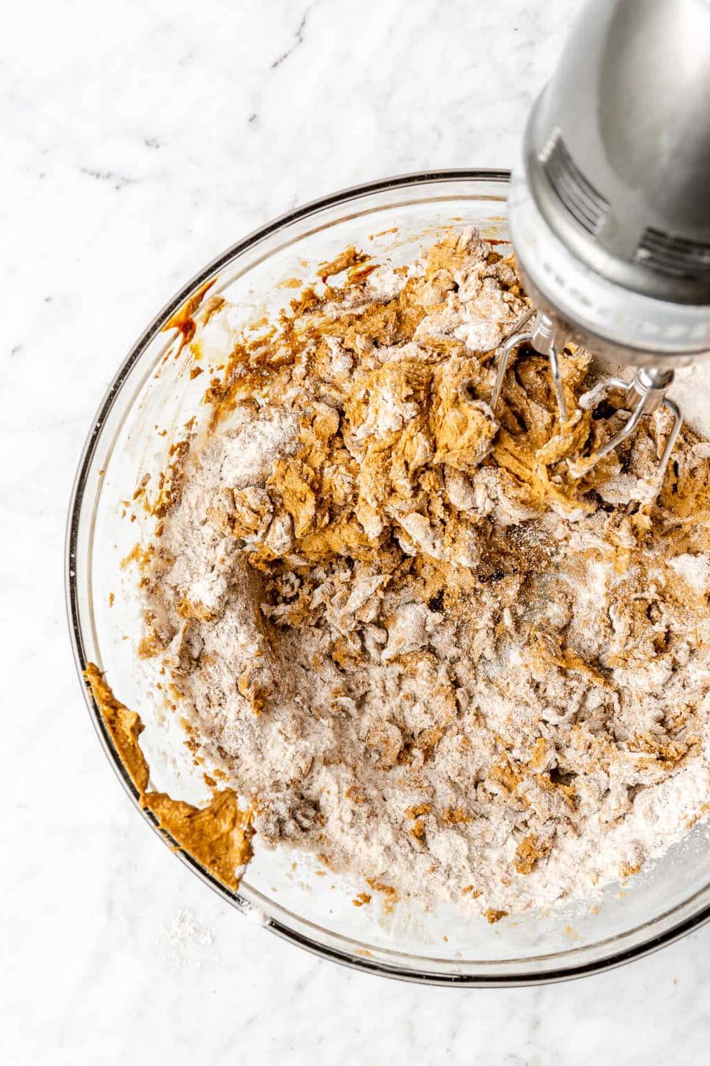 220817_Rum Raisin Cookies-27 Trockene Zutaten werden mit einem Handmixer in feuchte Zutaten in einer Glasschüssel eingearbeitet. Der Teig ist goldbraun.