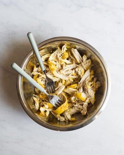 210423_Healing Tumeric Soup-25 Eine Schüssel mit zerkleinertem, leicht gelbem Hähnchenfleisch von Kurkuma und zwei Gabeln darin
