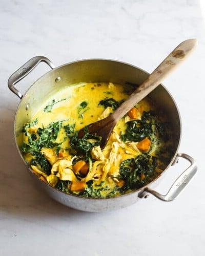 210423_Healing Tumeric Soup-29 Ein großer Topf mit heilender Kurkuma-Hühnersuppe und einem Holzlöffel darin