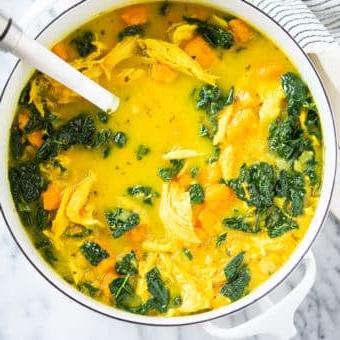 Hühnersuppe mit Ingwer und Kurkuma 5 Gelbe Kurkuma-Hühnersuppe mit Süßkartoffeln und Grünkohl in einem weißen Topf auf einer Marmoroberfläche