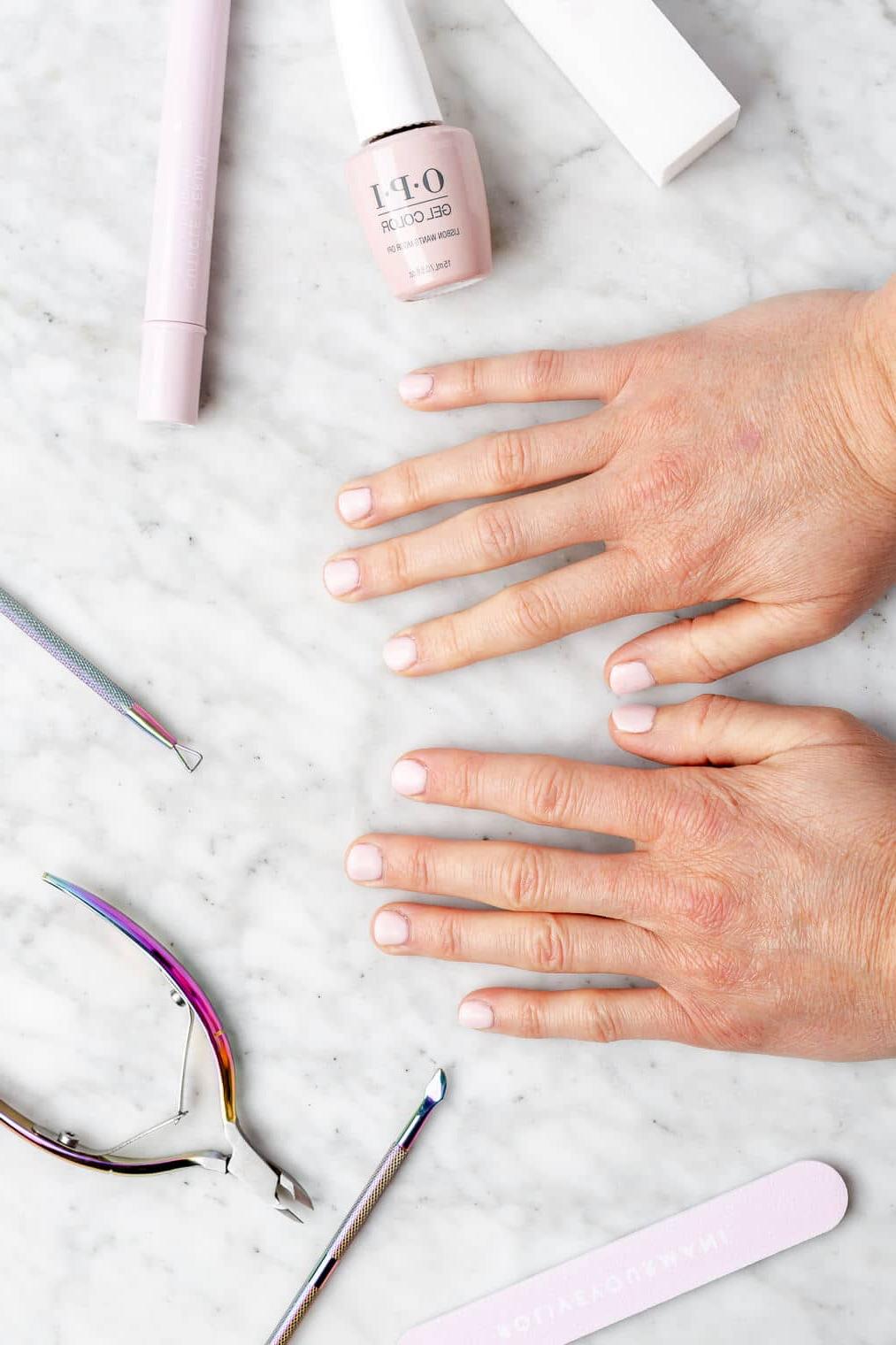 220831_Gel Manicure-14 Hände mit hellrosa lackierten Nägeln auf einer grau-weiß marmorierten Oberfläche, umgeben von Nagelwerkzeugen.