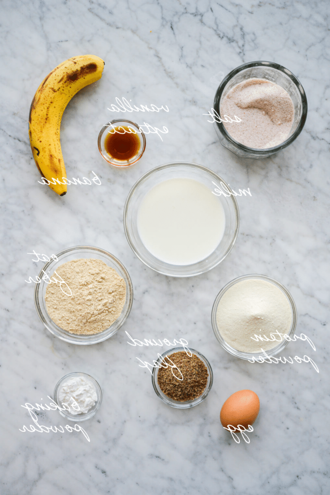 Wie man Protein-Pfannkuchen zubereitet 3 Beschriftete Zutaten für Protein-Pancakes in Schüsseln auf einer Marmoroberfläche.