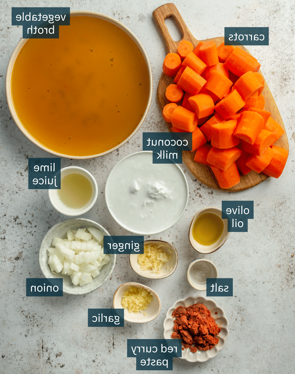 Thailändische Karotten-Ingwer-Suppe 3 Alle Zutaten für die Thai-inspirierte Karottensuppe, portioniert in Schalen auf einer grauen Steinoberfläche.