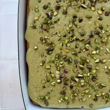 Pistazienkuchen mit Quarkcreme 3 Nahaufnahme eines Stücks Pistazienkuchen mit üppiger Hüttenkäse-Glasur und gehackten Pistazien darauf.