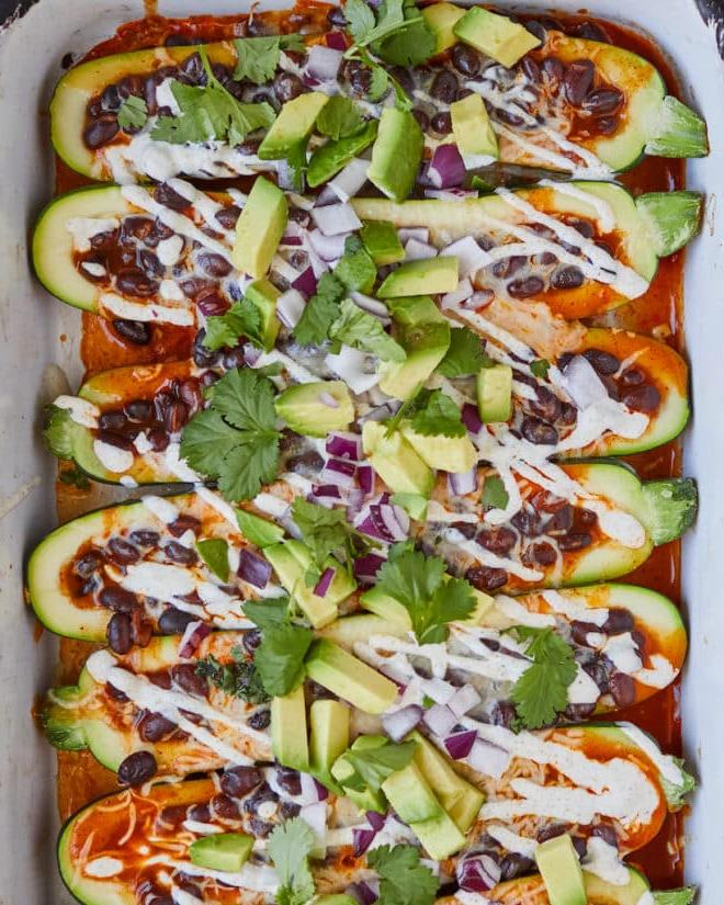 Zwei Abendessen mit schwarzen Bohnen 3 Enchilada-gefüllte Zucchiniboote, garniert mit Sauerrahm, Avocado und Koriander