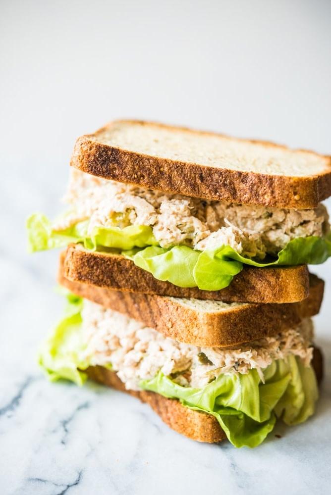 Klassisches Thunfischsalat-Rezept 3 Klassische Thunfischsalat-Sandwiches übereinander gestapelt auf einem Marmorbrett