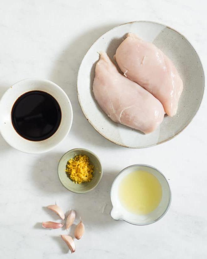 Alle Zutaten für eine Grillhähnchen-Marinade in verschiedenen Schüsseln auf einer Marmoroberfläche