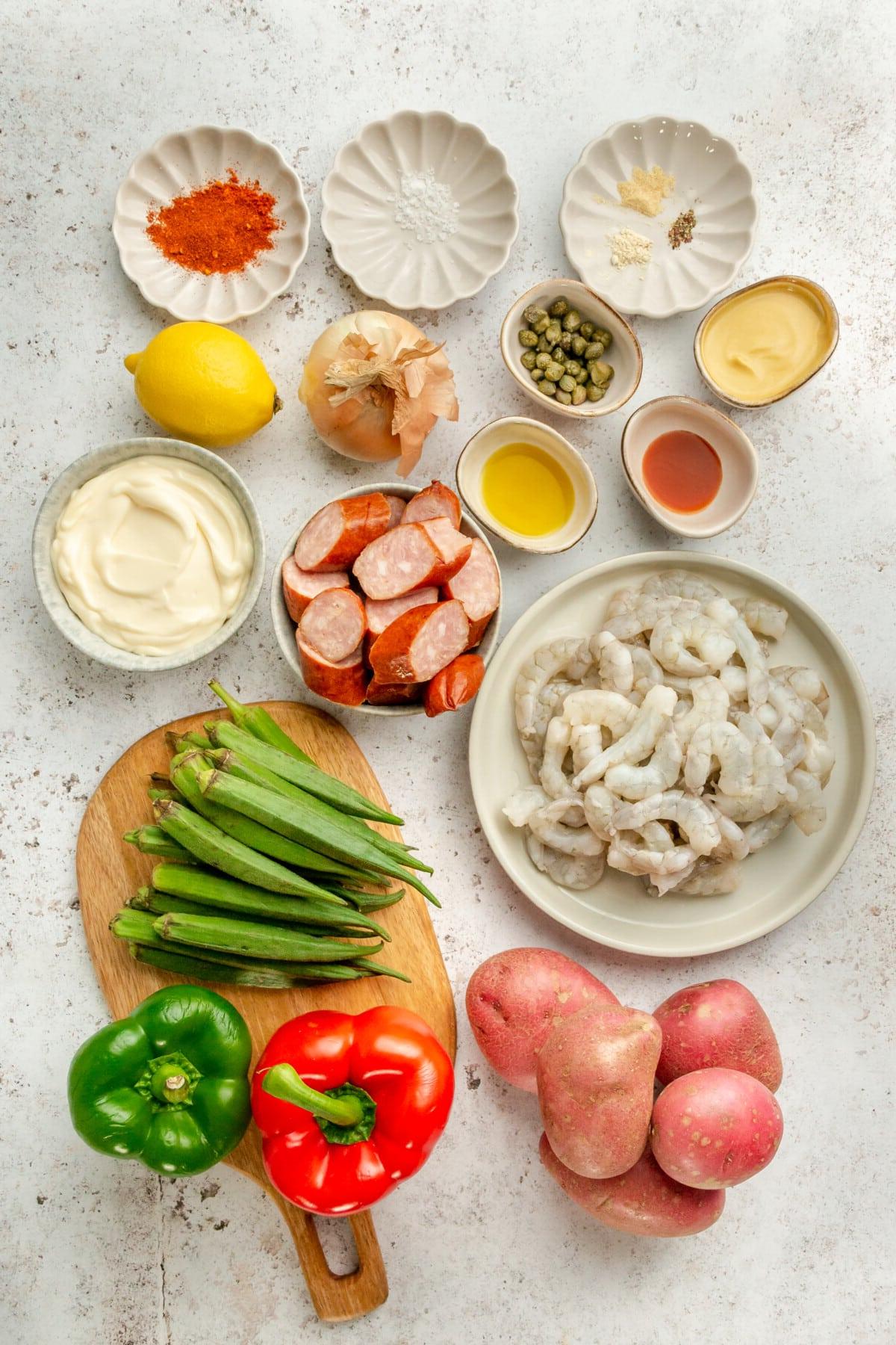 Cajun Garnelen vom Backblech 3 Zutaten für Cajun Garnelen-Ofenblech-Gericht in verschiedenen Schüsseln und Tellern auf hellem Untergrund arrangiert