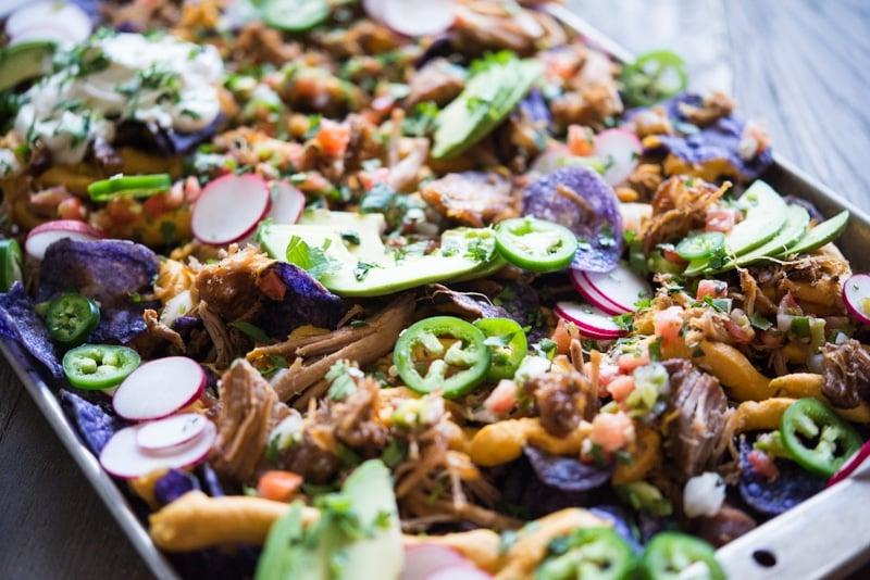 Nahaufnahme von Carnitas Nachos mit frischen Radieschen, Jalapenos und Pico de Gallo.