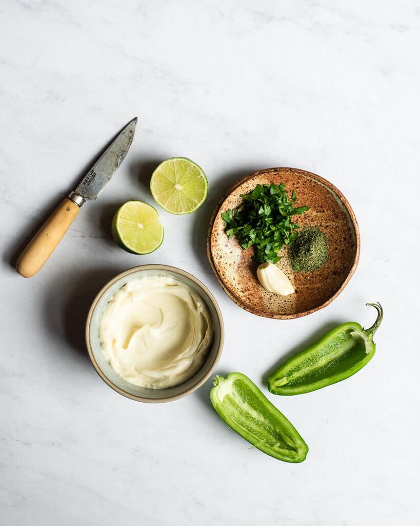 Jalapeño-Ranch-Dressing 3 Alle Zutaten für ein selbstgemachtes Jalapeño Ranch Dressing in verschiedenen Schalen und auf Tellern auf einer Marmoroberfläche.