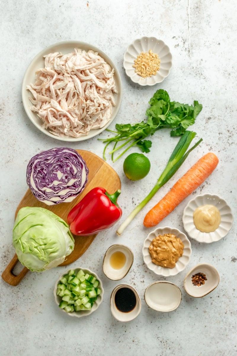 Thai-inspirierter Erdnuss-Hähnchensalat 3 Zutaten für den Thai-inspirierten Hähnchensalat in verschiedenen Schüsseln auf einer hellgrauen Arbeitsplatte.