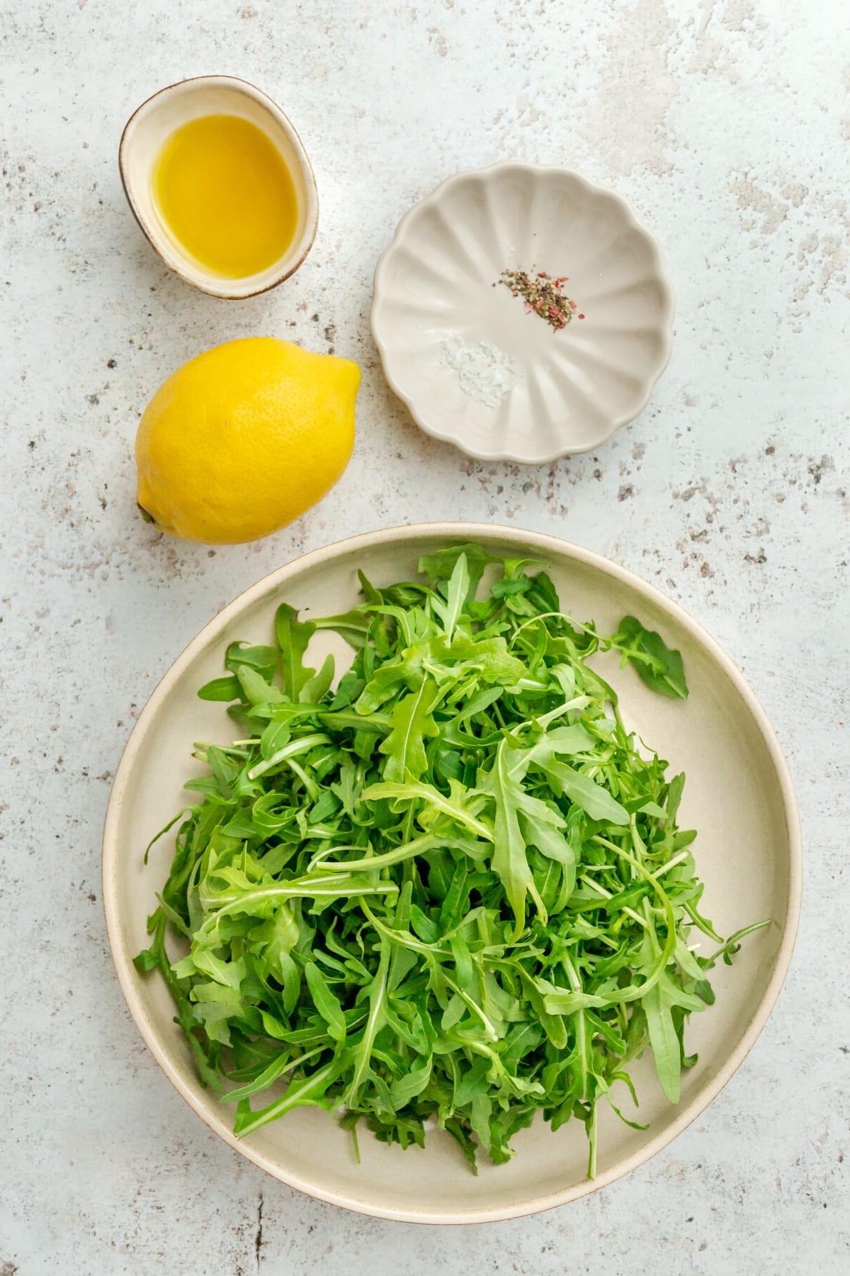 Rucola Salat mit Zitrone und Meersalz 3 Zutaten für Rucola Salat in verschiedenen Schalen auf hellem Hintergrund