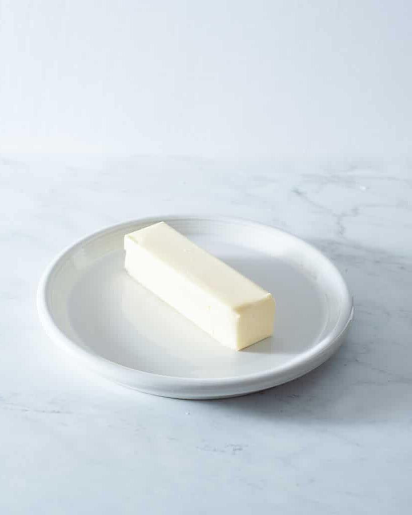 210920_How to Soften Butter-11 Ein Stück Butter auf einem kleinen weißen Teller