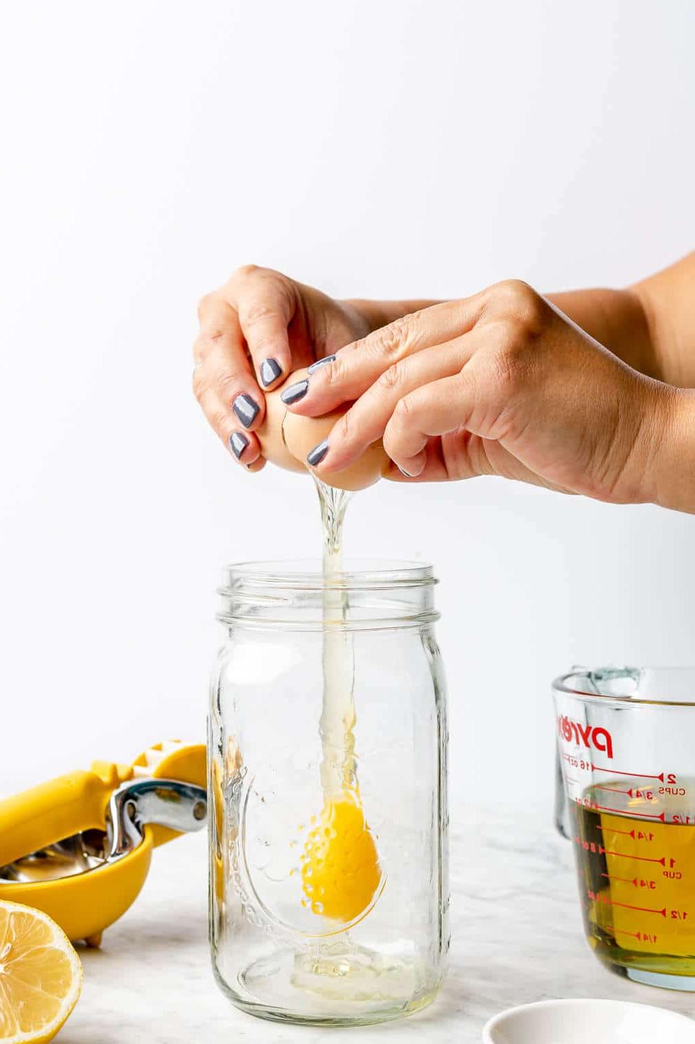 Zubereitungsschritt 1: Ei ins Glas geben Hand, die Ei in ein großes Einmachglas aufschlägt.