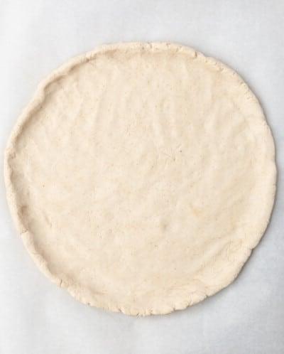 Pizzateig auf Backpapier ausgebreitet, bevor er mit Pizzabelag belegt wird