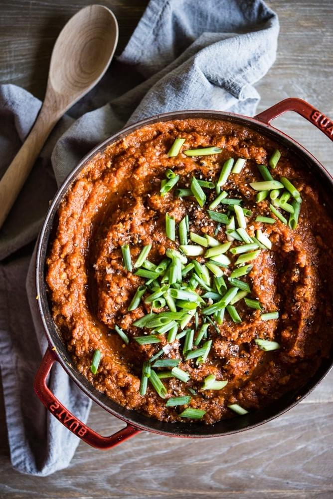 Ein großer roter Emailletopf gefüllt mit einem tief orangefarbenen Kürbis-Chili, garniert mit geschnittenen Frühlingszwiebeln.