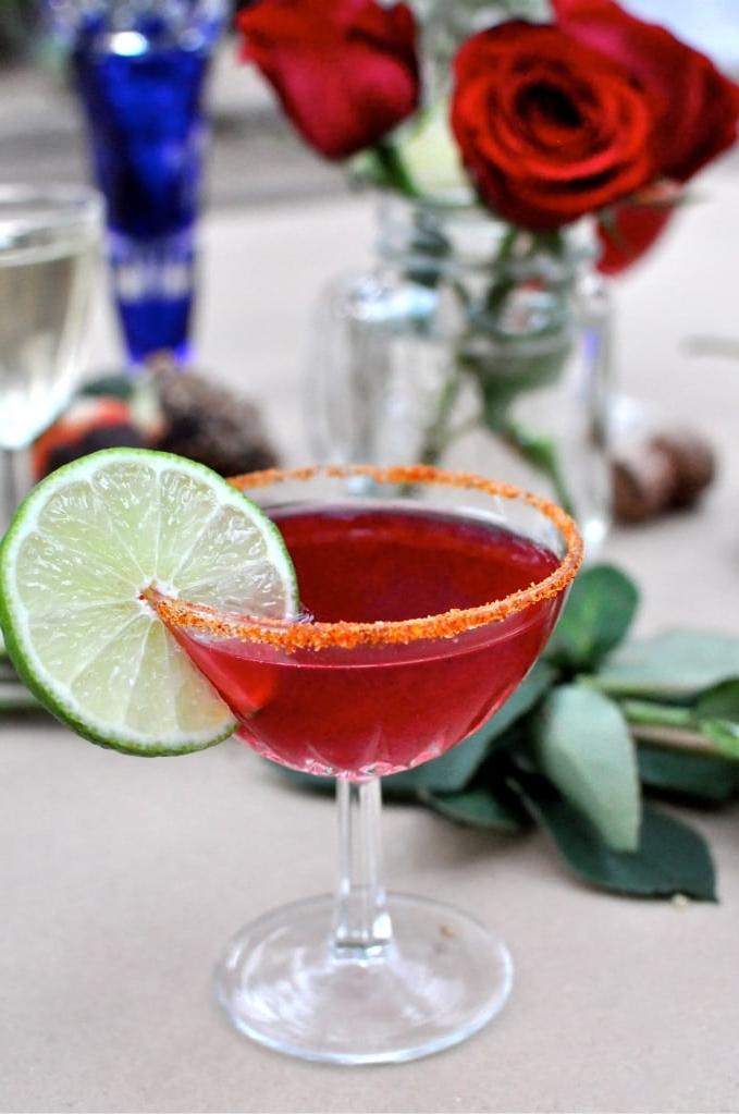 Nahaufnahme eines würzigen Granatapfel Martinis mit Chilipulver-Rand und Limettenscheibe.