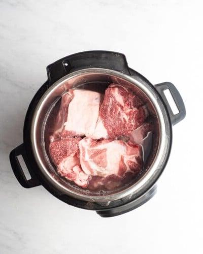 Ein Instant Pot mit Wasser und Stücken von roher Schweineschulter darin