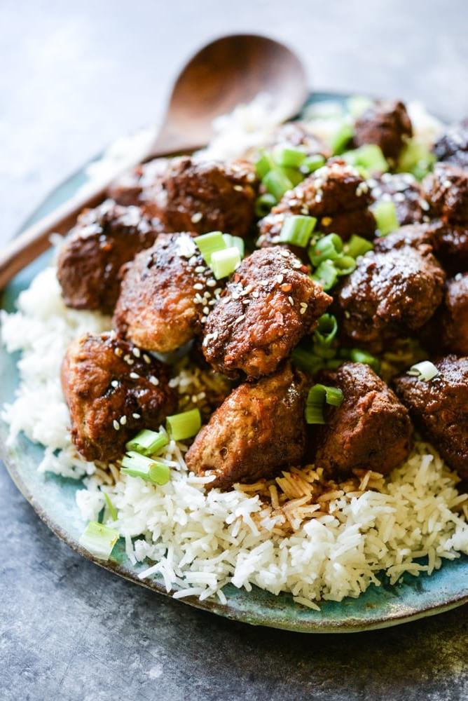 Puten-Teriyaki-Hackbällchen aus dem Schongarer 4 Teriyaki-Puten-Hackbällchen auf einem Bett aus Reis auf einem blauen Teller mit einem hölzernen Servierlöffel