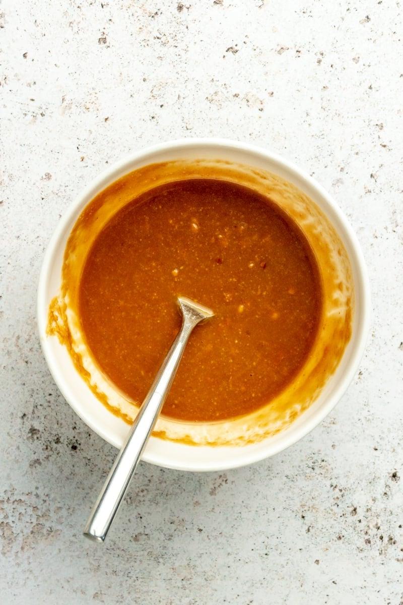 Thai-inspirierter Erdnuss-Hähnchensalat 4 Eine orangefarbene, cremige Mischung in einer weißen Schüssel mit einem Metalllöffel.