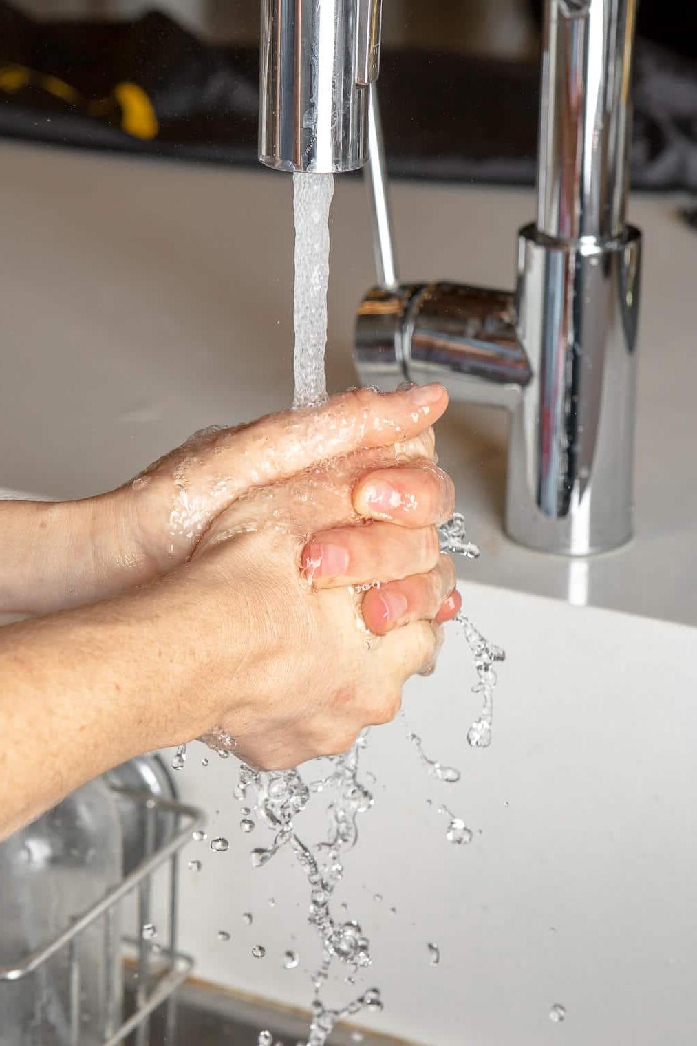 220831_Gel Manicure-04 Hände werden in einem Waschbecken mit weißer Arbeitsplatte gewaschen.