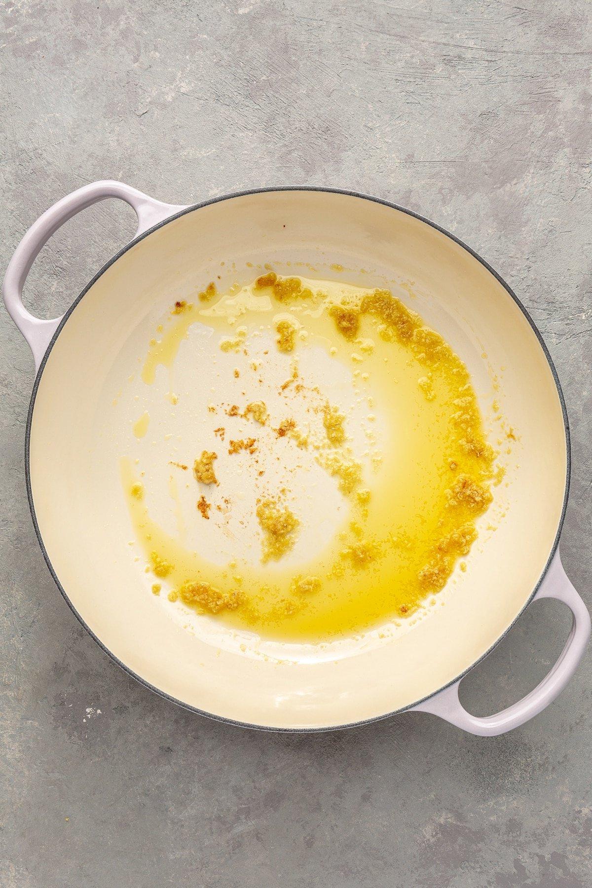 Ghee und gehackter Knoblauch wurden in einen weißen emaillierten Topf gegeben. Das Ghee ist geschmolzen und der gehackte Knoblauch leicht goldbraun geröstet.