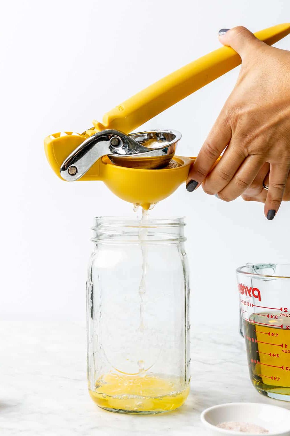 Zubereitungsschritt 2: Frischen Zitronensaft hinzufügen Hände, die eine Zitruspresse halten, um Zitronensaft über einem aufgeschlagenen Ei in ein großes Einmachglas zu pressen.