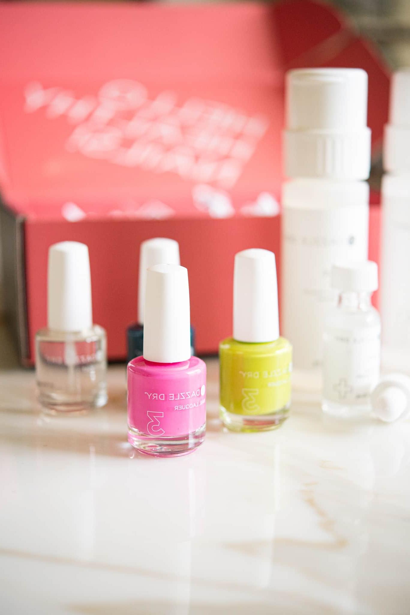 Dazzle Dry Nail System Rezension 5 Ein Set aus pinkem Nagellack mit gelbem und klarem Lack dahinter, kunstvoll positioniert vor einer passenden pinken Box – das Dazzle Dry Nagelsystem in seiner ganzen Pracht.