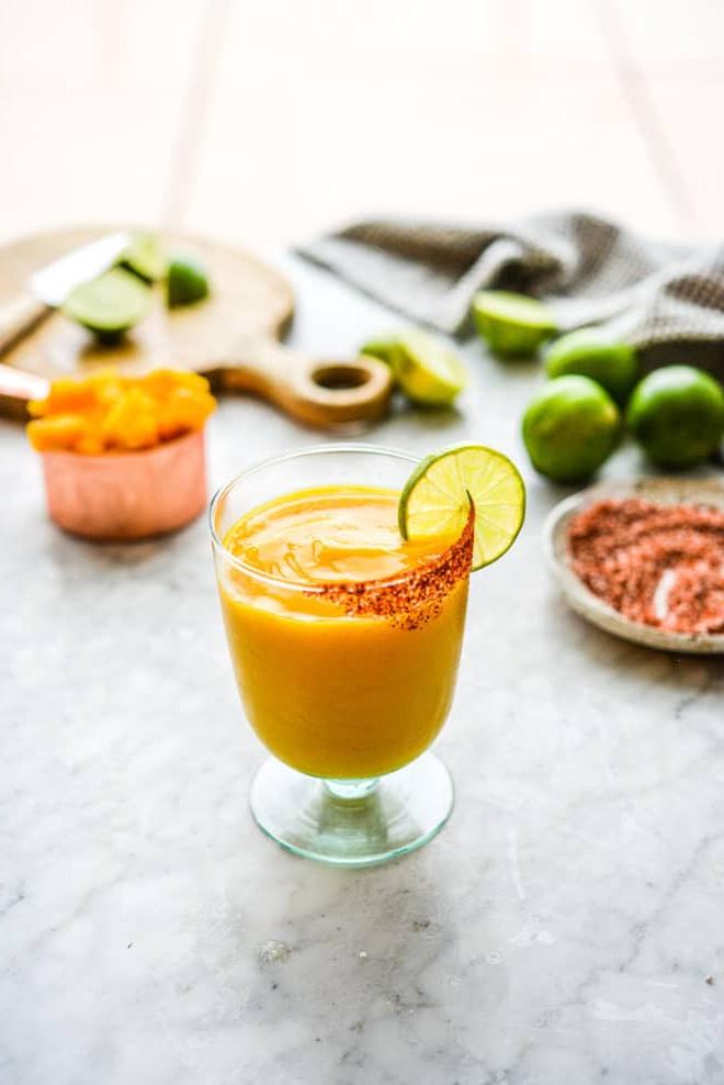 Einfaches Mango-Margarita-Rezept (Gefroren und auf Eis) 5 Ein Glas Frozen Mango Margarita mit Chilischnee-Rand, Zutaten für Mango Margaritas im Hintergrund