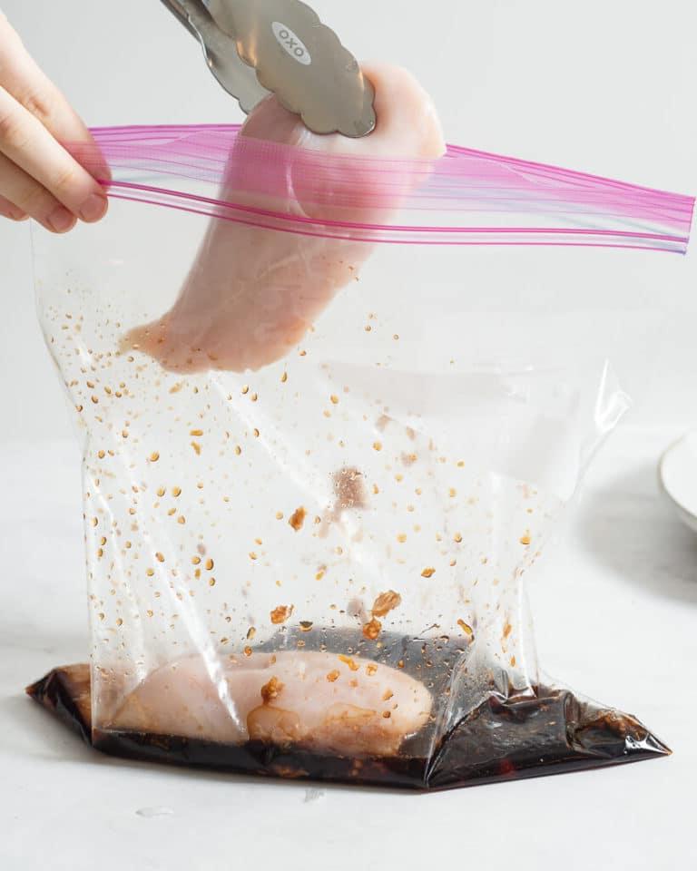 Eine Person fügt rohe Hähnchenbrüste in einen großen Zipper-Beutel mit Grillhähnchen-Marinade hinzu