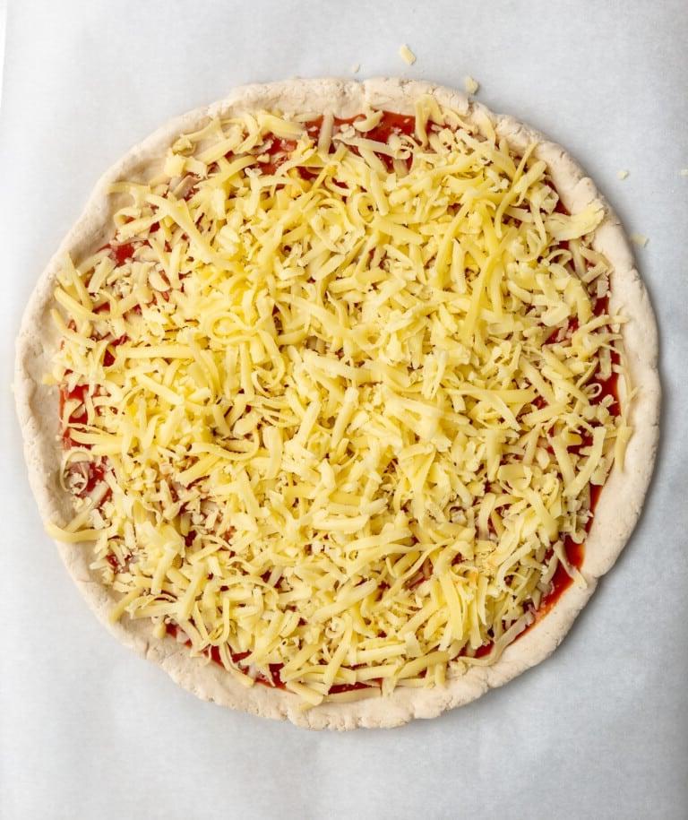 Roher Pizzateig belegt mit BBQ-Sauce und Mozzarella-Käse.