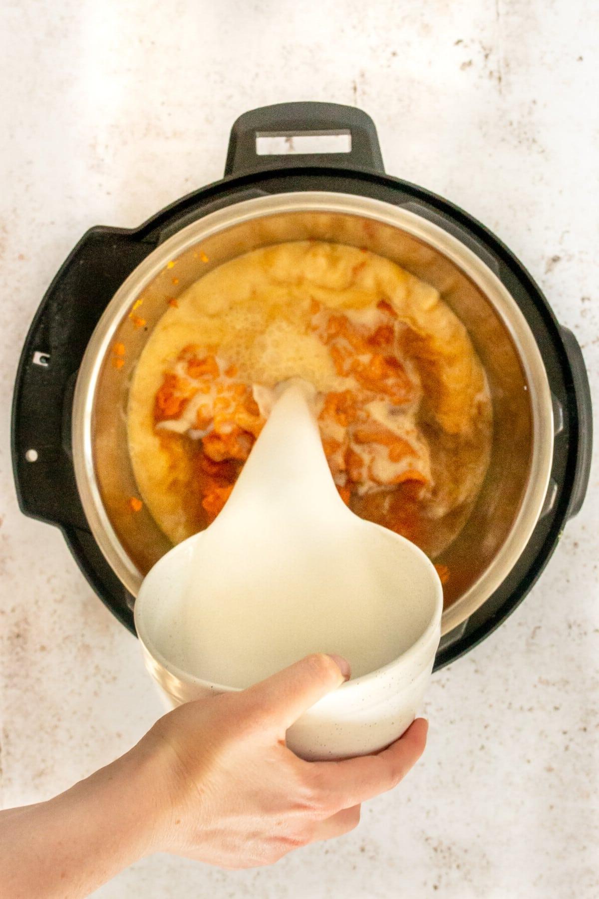 Kokosmilch wird zusammen mit Kürbis, Brühe und Kräutern in einen Instant Pot auf hellem Untergrund gegossen.