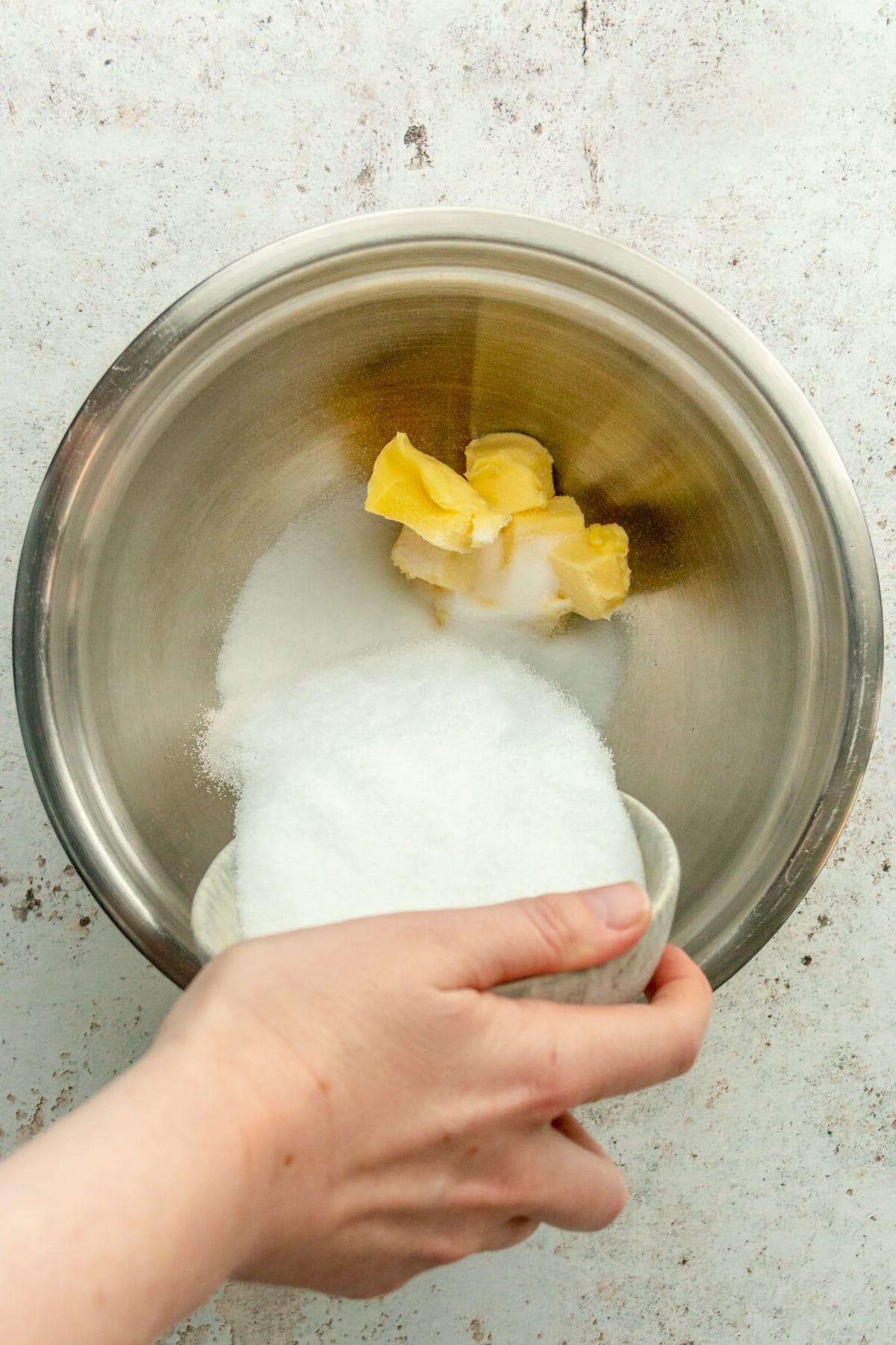**Weiße Schokoladen-Pfefferminz-Kühlschrankkekse** 5 Zucker wird über Butterwürfel in einer Edelstahlschüssel auf hellem grauem Untergrund gegeben.