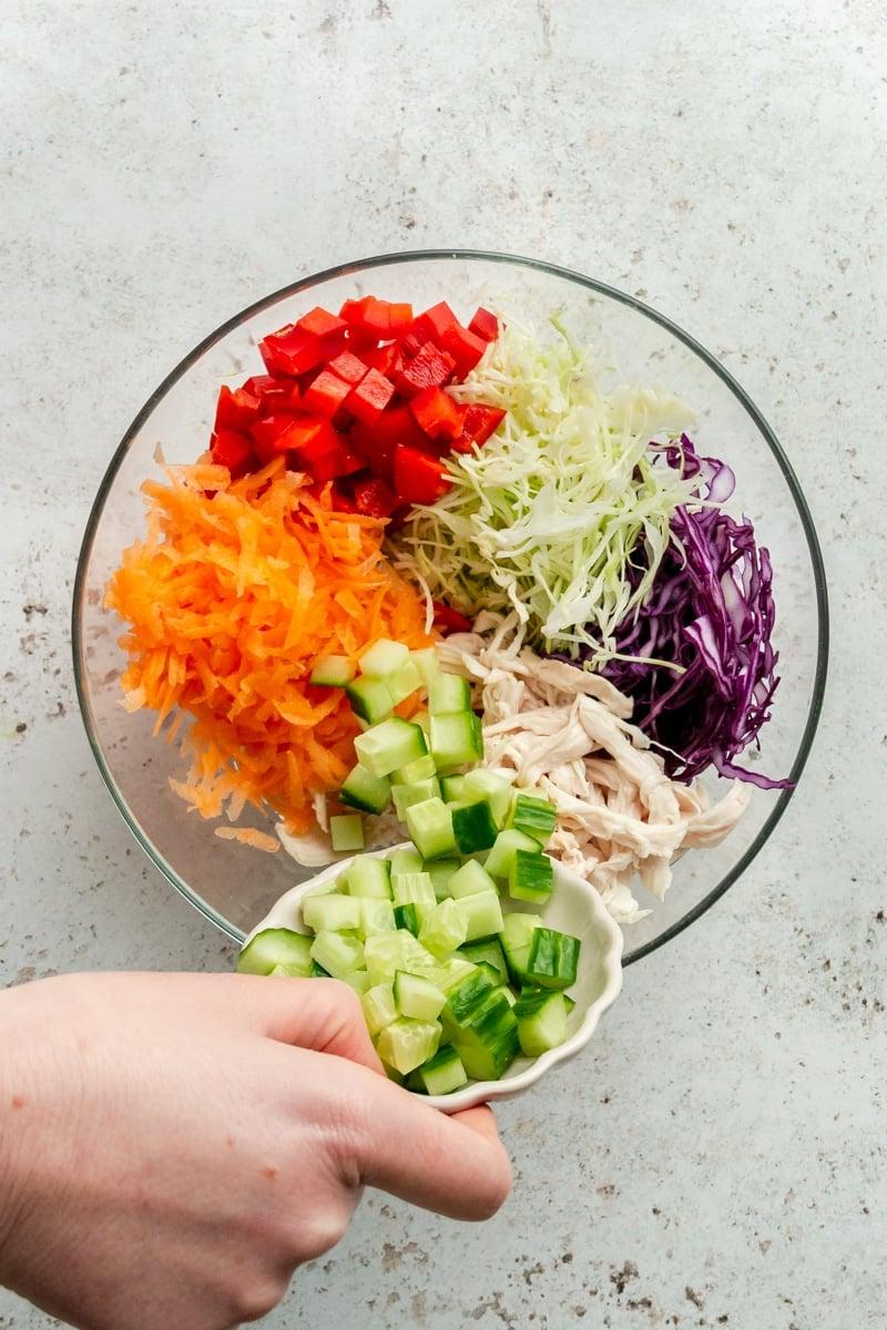 Thai-inspirierter Erdnuss-Hähnchensalat 5 Gehacktes Gemüse wird in eine große Glasschüssel geschüttet.