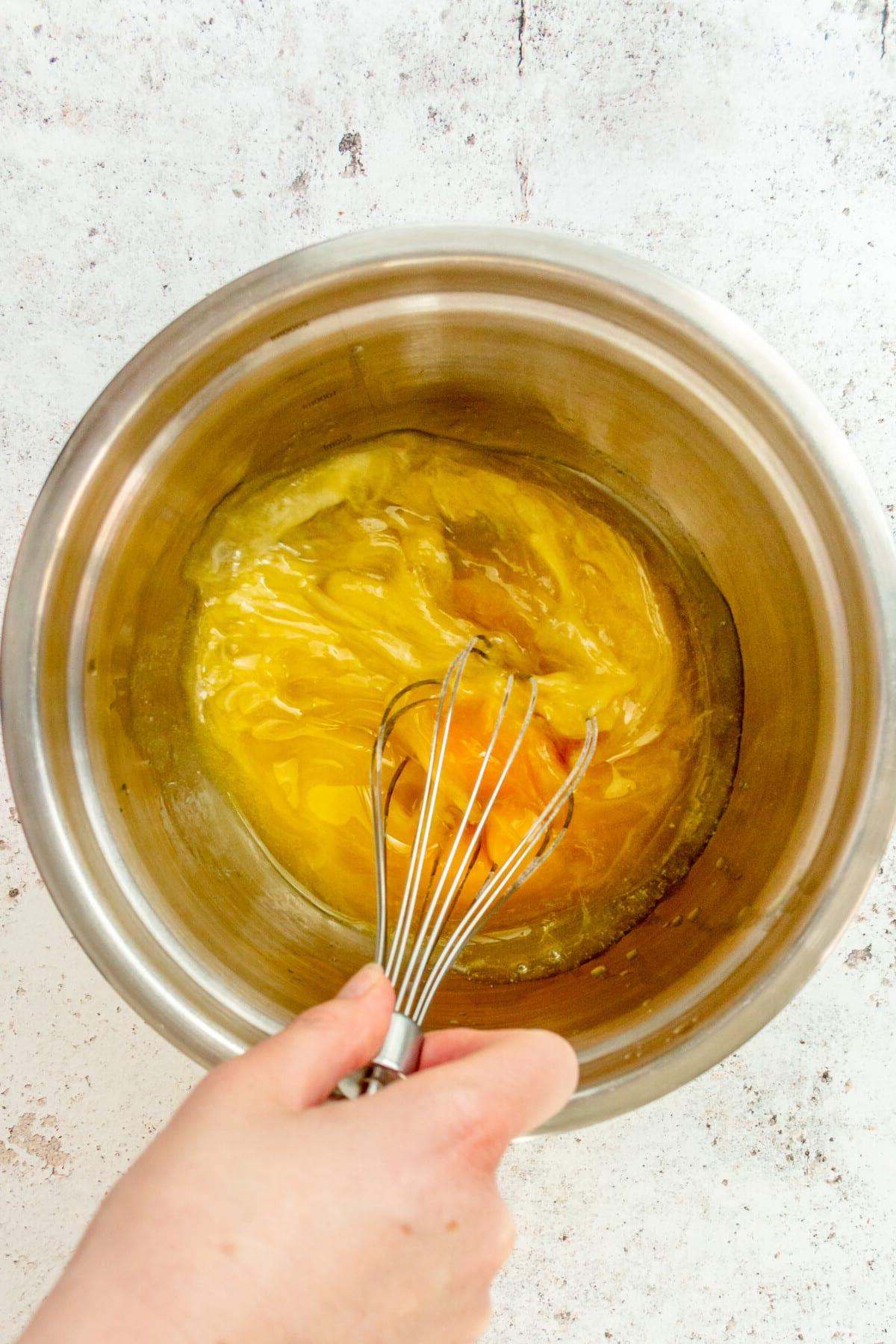 **Paläo Apfel-Zimt-Muffins** 5 An egg and butter mixture is whisked in a stainless steel bowl on a light grey surface.