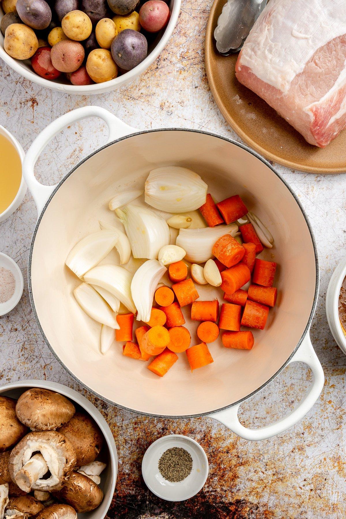 **Balsamico-Schweinelendenrezept** 5 Stücke von leuchtend orangefarbenen Karotten und geschnittenen weißen Zwiebeln wurden in einen weißen, emaillierten Topf gelegt.