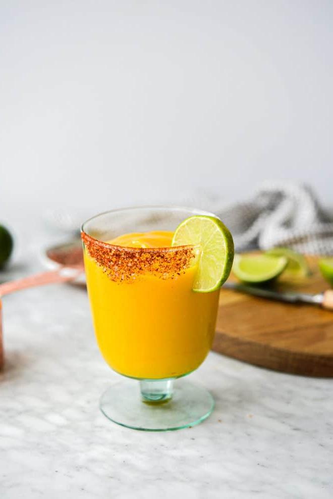 Einfaches Mango-Margarita-Rezept (Gefroren und auf Eis) 6 Ein Glas Frozen Mango Margarita mit Chilischnee-Rand, Zutaten für Mango Margaritas im Hintergrund