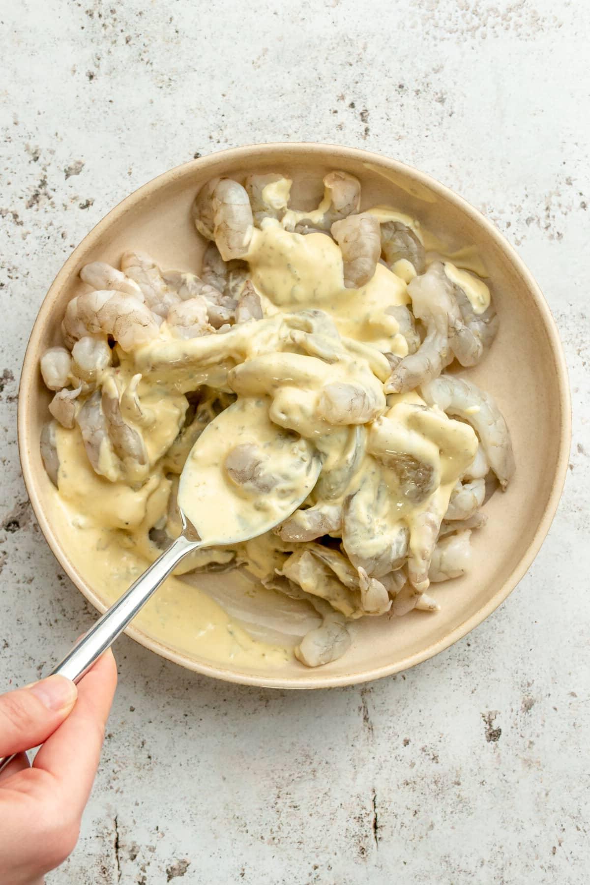 Cajun Garnelen vom Backblech 6 Garnelen werden in einer flachen Keramikschale durch Remouladensoße gewendet.