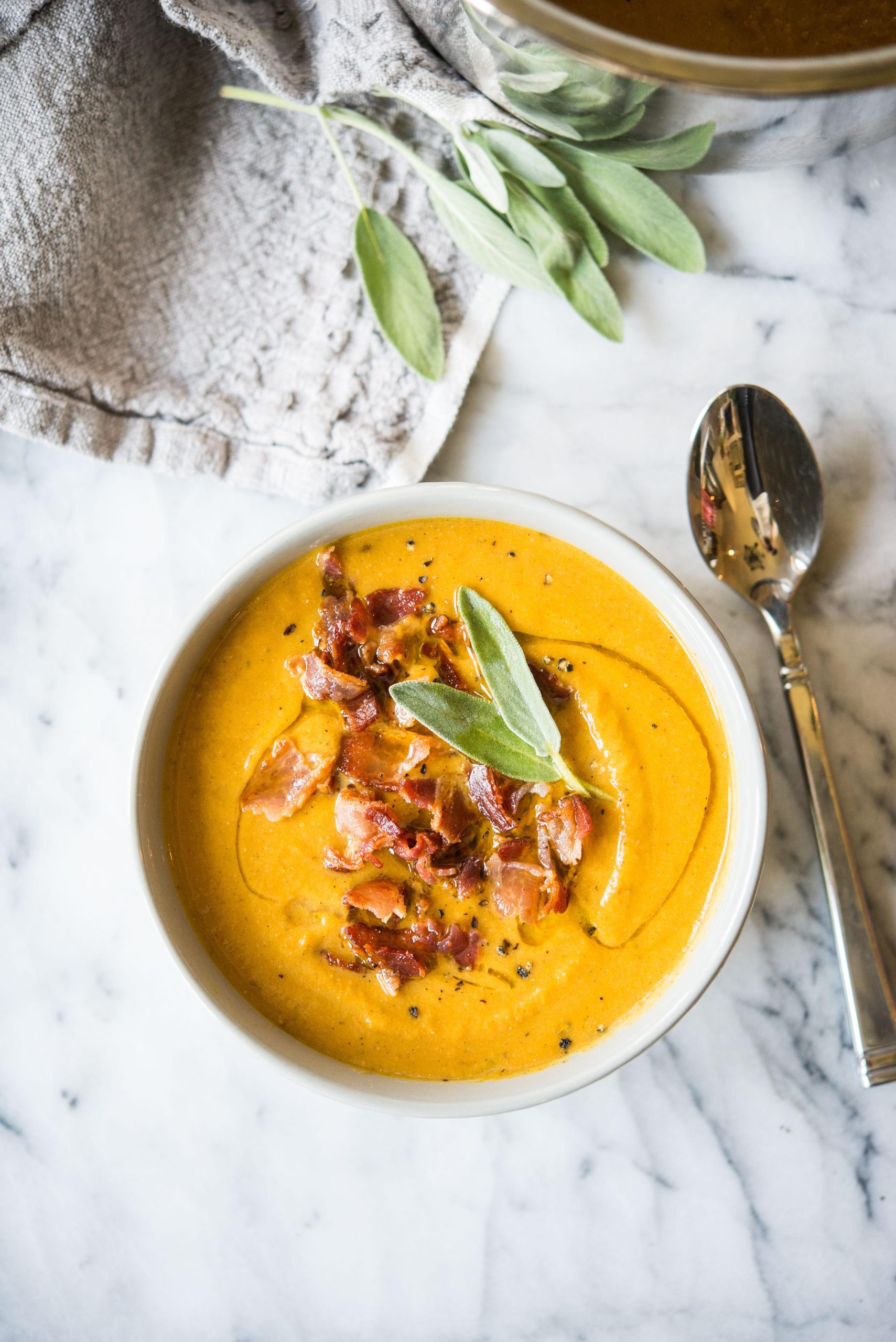 Kürbissuppe, belegt mit Speck und Salbei, in einer grauen Schüssel auf einem Marmorbrett