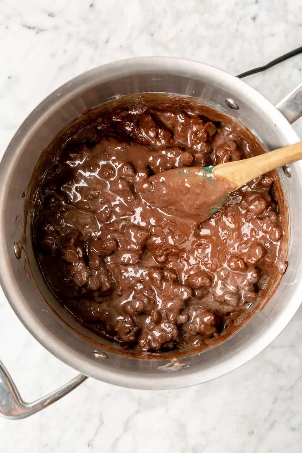 Löffel rührt schmelzende Schokoladenstückchen und gezuckerte Kondensmilch in einem Topf zusammen.
